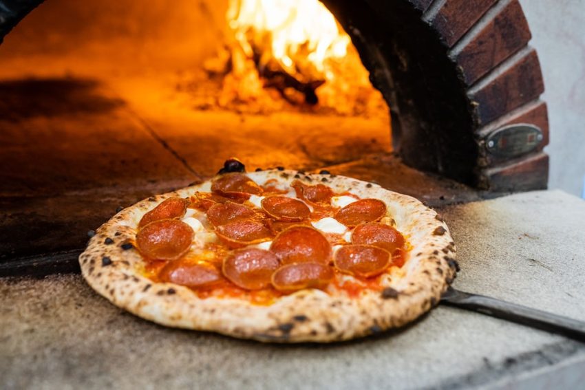 pepironii pizza infront of a wood oven