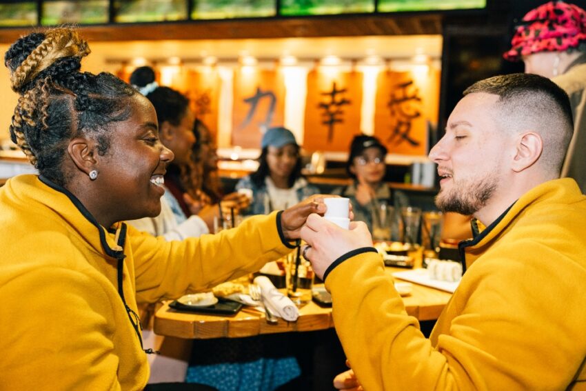 Two people in yellow shirts toast with sake in Geisha Scotssdale